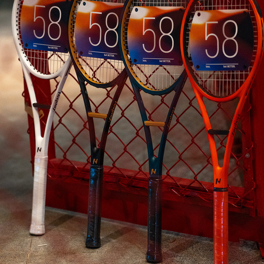 Four Nisplay 58 Sweet Spot Trainers in different colors beside a tennis court fence