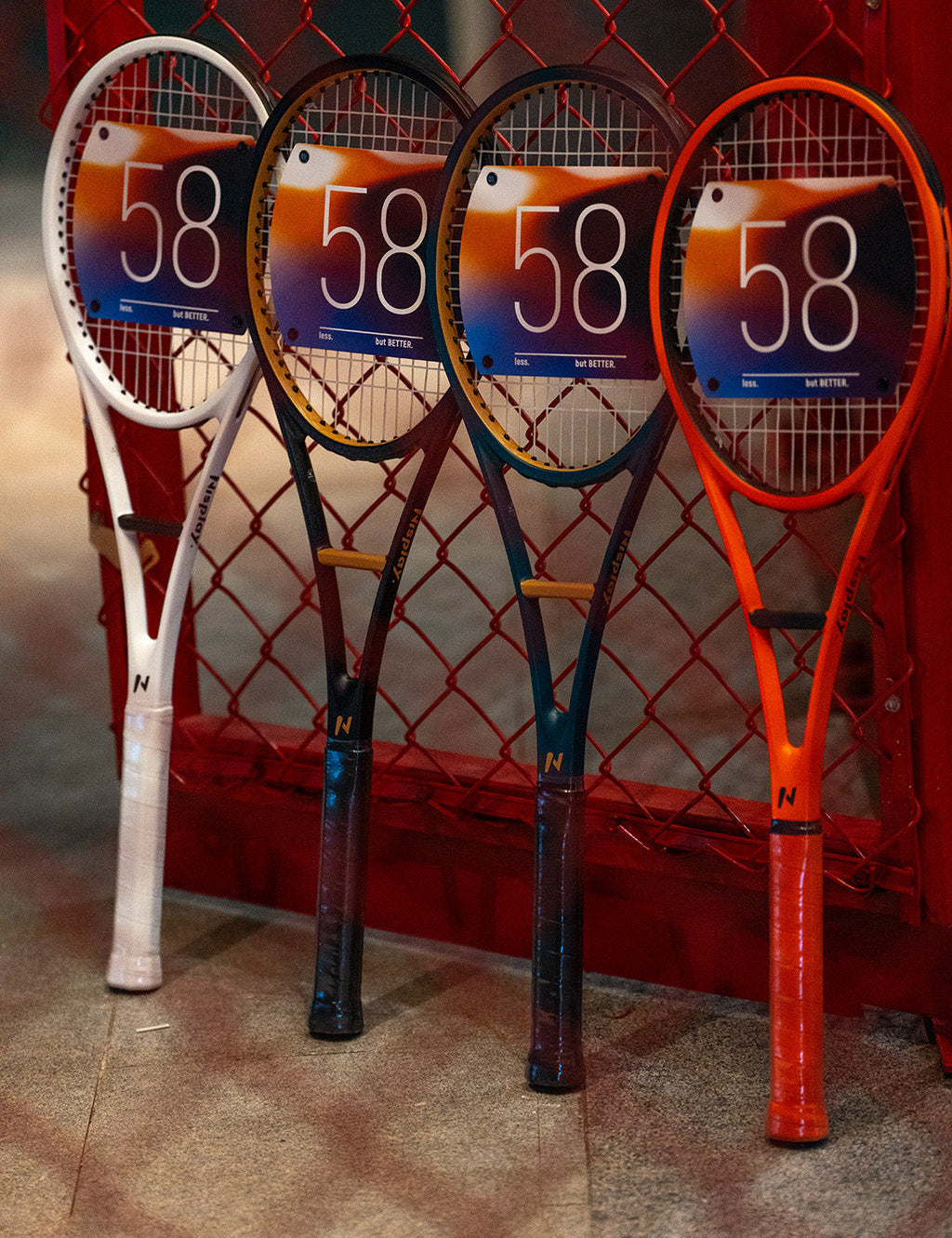 Four Nisplay 58 Sweet Spot Trainers in different colors beside a tennis court fence