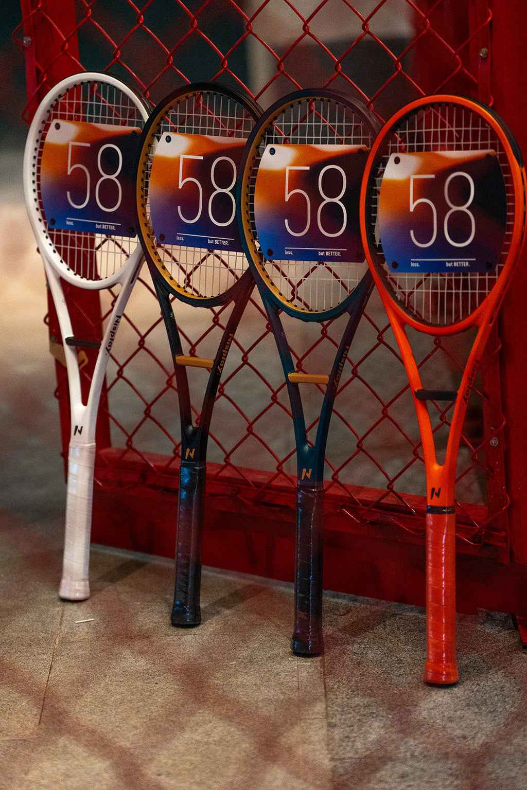 Four Nisplay 58 Sweet Spot Trainers in different colors beside a tennis court fence
